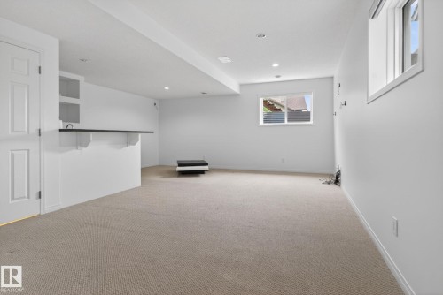 Carpeted lower level featuring recessed lighting, a built-in bar with open shelving, and a prominent window providing natural illumination - 3806 Powell Wynd, Edmonton, AB 