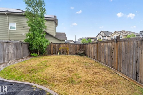 Fenced backyard featuring a paver stone patio border, wood privacy fencing, and a mature deciduous tree - 3806 Powell Wynd, Edmonton, AB 