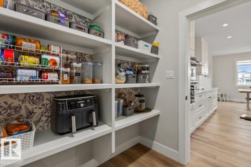 Walk-in pantry featuring extensive built-in shelving, decorative wall covering, and wood-finish flooring - 45 Elwyck Gate, Spruce Grove, AB 