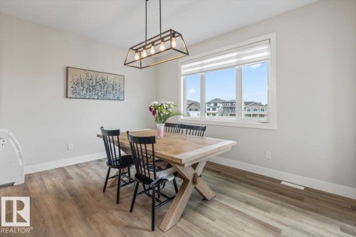 Dining area featuring wood-finish flooring, a large window with roller shades, and a linear black metal chandelier - 45 Elwyck Gate, Spruce Grove, AB 