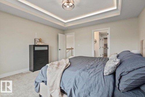 Bedroom featuring a tray ceiling with integrated lighting, a ceiling-mounted light fixture, light gray carpeting, and white baseboards - 45 Elwyck Gate, Spruce Grove, AB 