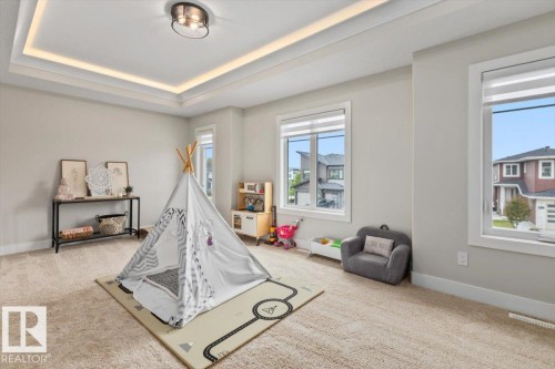 Spacious room featuring tray ceiling with recessed lighting, light neutral wall paint, two large windows, and carpet flooring - 45 Elwyck Gate, Spruce Grove, AB 