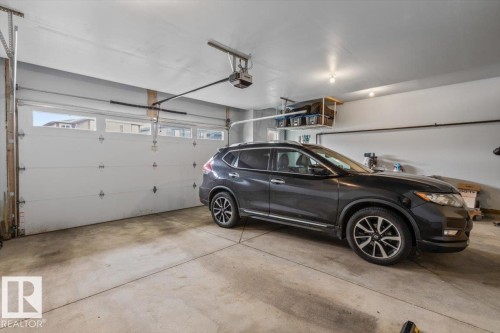 Attached garage featuring a concrete floor, automatic garage door opener, overhead lighting, and built-in overhead storage shelves - 45 Elwyck Gate, Spruce Grove, AB 