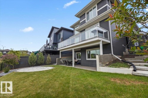 Spacious backyard with a grass lawn, circular paver patio, and stone retaining wall - 45 Elwyck Gate, Spruce Grove, AB 