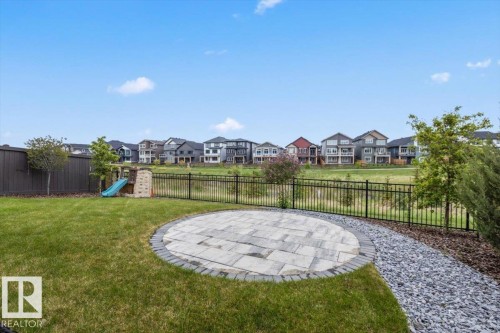 Expansive backyard featuring a circular paver patio, a gravel pathway, a black metal fence, a dark wood fence, and mature trees - 45 Elwyck Gate, Spruce Grove, AB 