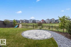 Expansive backyard featuring a circular paver patio, a gravel pathway, a black metal fence, a dark wood fence, and mature trees - 