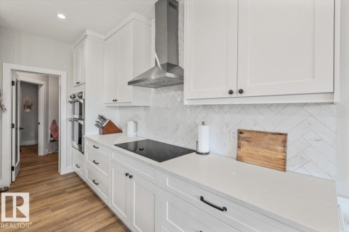 Kitchen featuring white shaker cabinetry, light-toned countertops, a herringbone tile backsplash, stainless steel double wall ovens, and wood-finish flooring - 45 Elwyck Gate, Spruce Grove, AB 
