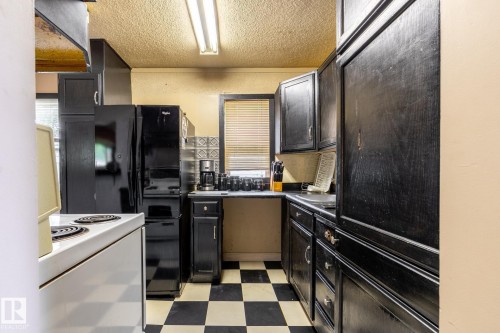 Compact kitchen featuring black cabinetry, a black and white checkered floor, a built-in black refrigerator, a black electric range, and a window with blinds - 5919 121 Avenue, Edmonton, AB 