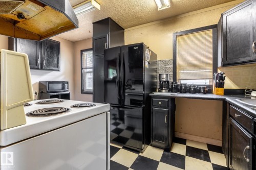 Kitchen featuring black and white checkerboard flooring, black cabinetry, black appliances, and a window with horizontal blinds - 5919 121 Avenue, Edmonton, AB 