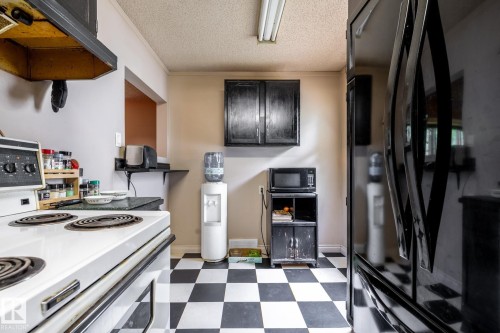 Kitchen area featuring black and white checkerboard flooring, a white electric range, and black upper cabinetry - 5919 121 Avenue, Edmonton, AB 