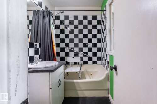 Bathroom featuring a checkered tile shower surround, window, and a white vanity with a dark countertop - 5919 121 Avenue, Edmonton, AB 