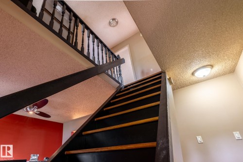 Hardwood tread staircase with dark risers and balusters, featuring textured ceiling finishes and overhead lighting - 5919 121 Avenue, Edmonton, AB 