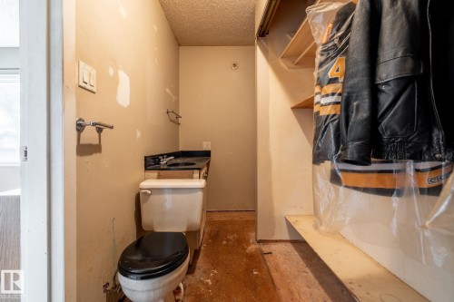 Compact powder room featuring a toilet with a black seat, a black vanity countertop with an integrated sink, and an exposed wood subfloor - 5919 121 Avenue, Edmonton, AB 