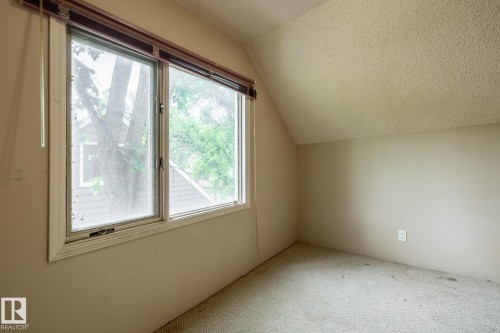 Carpeted room featuring a large window, sloped ceiling, and textured ceiling finish - 5919 121 Avenue, Edmonton, AB 