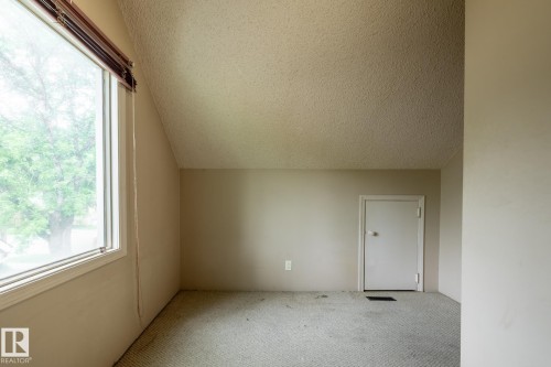 Attic space featuring a large window, sloped ceiling, light-colored walls, patterned carpet flooring, and a white door - 5919 121 Avenue, Edmonton, AB 