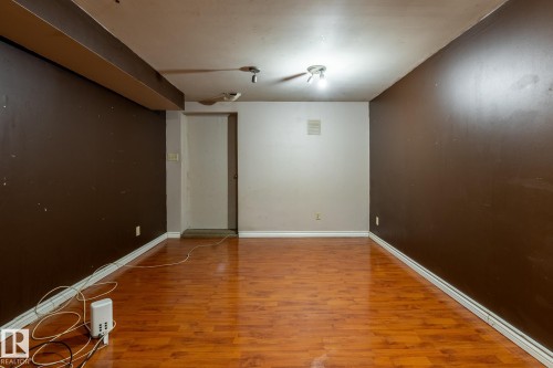 Spacious room featuring wood-finish flooring, white baseboards, and a neutral ceiling - 5919 121 Avenue, Edmonton, AB 