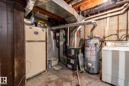 Furnace, water heater, and laundry appliances in a utility area featuring exposed wood joists and concrete walls - 5919 121 Avenue, Edmonton, AB 
