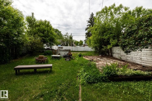 Spacious backyard featuring a grass lawn, mature trees, a fire pit area, and a concrete pad - 5919 121 Avenue, Edmonton, AB 
