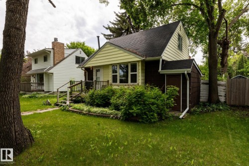 Charming residence featuring a light yellow facade, dark brown siding, and a prominent front porch - 5919 121 Avenue, Edmonton, AB 