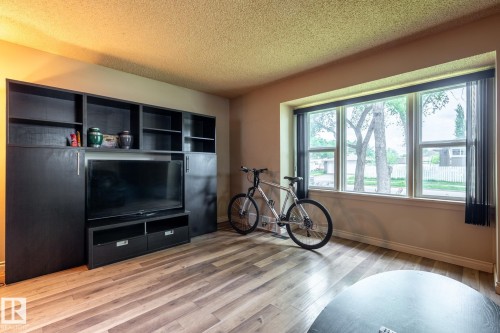 Spacious room featuring a multi-pane window with vertical blinds, wood-finish flooring, and a large built-in shelving unit with cabinet storage - 5919 121 Avenue, Edmonton, AB 