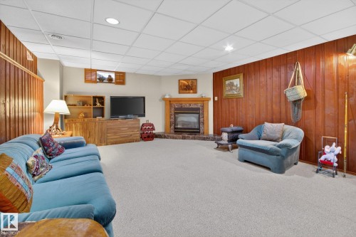 Spacious lower-level room featuring wood paneling, a gas fireplace with a tile surround, and a drop ceiling with recessed lighting - 9243 74 Street, Edmonton, AB 