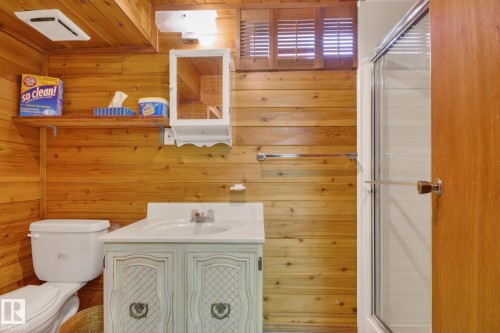 Bathroom featuring wood-paneled walls, a white vanity with decorative cabinetry, a white toilet, and a glass-enclosed shower - 9243 74 Street, Edmonton, AB 