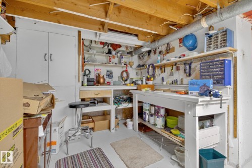 Dedicated workshop space featuring exposed ceiling joists, ample built-in shelving, a sturdy workbench, and a white storage cabinet - 9243 74 Street, Edmonton, AB 