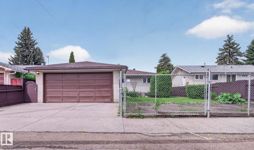 Detached garage featuring a paneled garage door, concrete driveway, and exterior lighting - 9243 74 Street, Edmonton, AB 