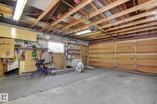 Garage interior featuring exposed ceiling joists, concrete flooring, and a paneled garage door - 9243 74 Street, Edmonton, AB 