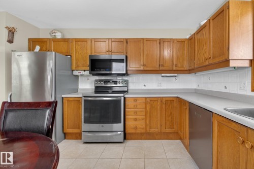 U-shaped kitchen featuring wood cabinetry, light-toned countertops, and a white tile backsplash - 9243 74 Street, Edmonton, AB 