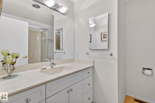Bathroom vanity featuring a light-toned countertop with an integrated sink, white cabinetry with silver-tone hardware, and an expansive wall mirror - 9243 74 Street, Edmonton, AB 