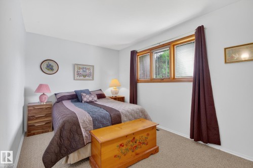 Bedroom featuring light neutral wall paint, carpet flooring, and a three-pane window with wood trim - 9243 74 Street, Edmonton, AB 