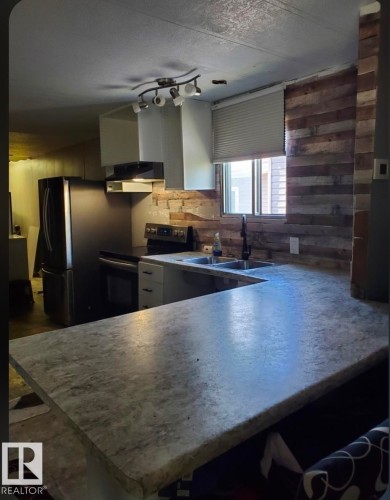 Kitchen featuring a U-shaped countertop, double basin sink, black appliances, track lighting, and wood plank wall accents - 14 Willowdale Drive, Edmonton, AB 