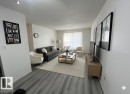 Spacious living area featuring wood-finish flooring, white walls, and a large window with sheer drapery - 212 2620 Mill Woods Road E, Edmonton, AB 
