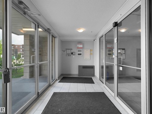 Entryway featuring commercial-grade glass doors with aluminum frames, white tiled flooring, and flush-mount ceiling lighting - 406 11820 22 Avenue, Edmonton, AB 