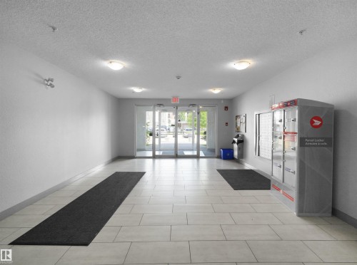 Light-toned tile flooring throughout the common area, featuring recessed lighting and wall-mounted fixtures - 406 11820 22 Avenue, Edmonton, AB 