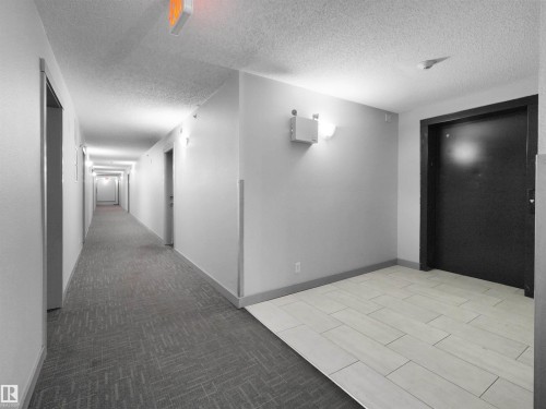 Long hallway featuring a patterned carpet runner, white ceiling, sconce lighting, and a light-toned tile landing - 406 11820 22 Avenue, Edmonton, AB 