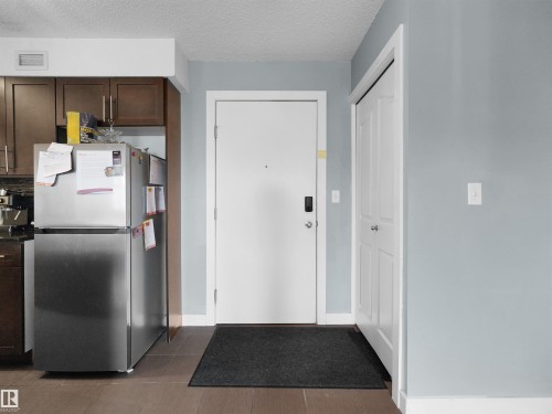 Entryway featuring wood-finish flooring, light blue wall paint, a white door with smart lock, and an adjacent closet with a paneled white door - 406 11820 22 Avenue, Edmonton, AB 