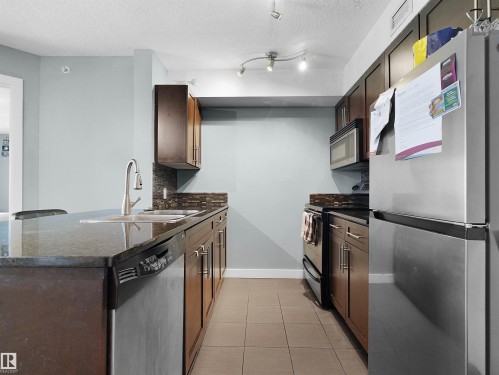 Kitchen featuring dark wood-finish cabinetry, stainless steel appliances, dark stone countertops, and a tile backsplash - 406 11820 22 Avenue, Edmonton, AB 