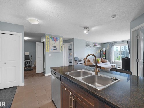 Kitchen island with a double basin stainless steel sink, brushed nickel faucet, and dark stone countertop - 406 11820 22 Avenue, Edmonton, AB 