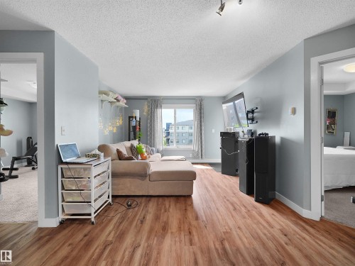 Spacious living area featuring wood-finish flooring, light blue walls, and track lighting - 406 11820 22 Avenue, Edmonton, AB 