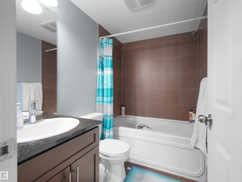 Full bathroom featuring a dark wood-finish vanity with an undermount sink, a dark countertop, and a tiled shower-tub combination with brown wall tiling - 406 11820 22 Avenue, Edmonton, AB 