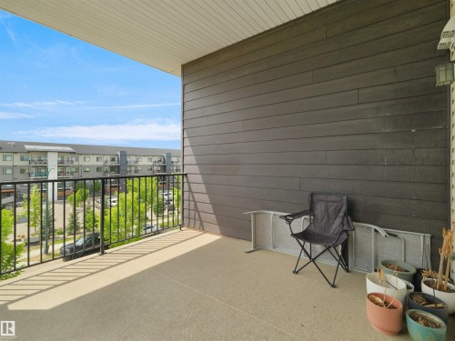 Spacious private balcony featuring a concrete surface, dark horizontal siding, a black metal railing, and an overhead soffit - 406 11820 22 Avenue, Edmonton, AB 