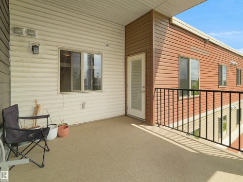 Private exterior balcony featuring a textured floor, white vinyl siding, a glass-paned door, and black metal railings - 406 11820 22 Avenue, Edmonton, AB 