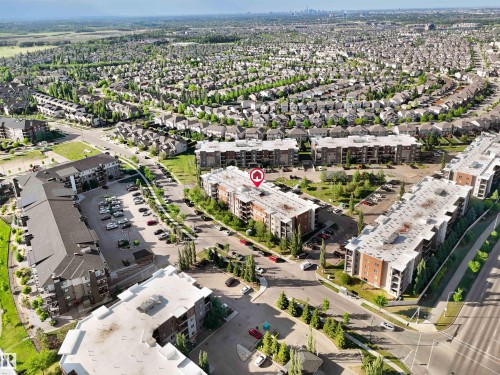 Aerial overview of a residential neighborhood featuring multiple multi-story apartment buildings with flat roofs and a dense arrangement of single-family homes with dark-pitched roofs - 406 11820 22 Avenue, Edmonton, AB 