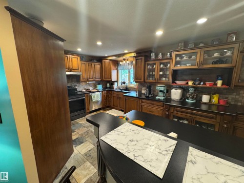 Kitchen featuring wood cabinetry with glass-front display uppers, dark countertops, and a tiled backsplash - 4502 55 Avenue, Vegreville, AB 