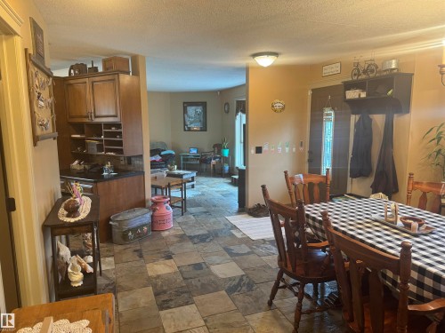 Inviting open-concept living space featuring slate-style flooring, a recessed kitchen area with wood cabinetry, and a dark wood entry door with decorative glass - 4502 55 Avenue, Vegreville, AB 