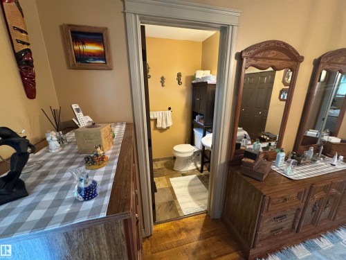 Bathroom featuring a white toilet, pedestal sink, and a dark wood-finish storage cabinet - 4502 55 Avenue, Vegreville, AB 