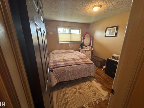 Bedroom featuring wood-finish flooring, a single window with blinds, and a flush-mount ceiling light fixture - 4502 55 Avenue, Vegreville, AB 