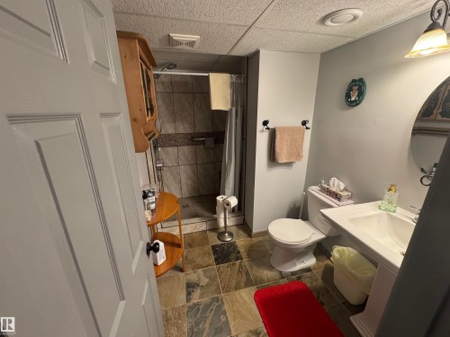 Bathroom featuring a pedestal sink, toilet, and tiled shower with a glass enclosure - 4502 55 Avenue, Vegreville, AB 